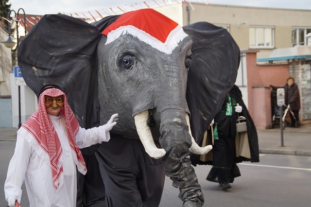 Man dressed as an Arab walking with another man dressed as elephant down street.