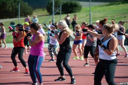 Numerous men and women doing an exercise routine outside.