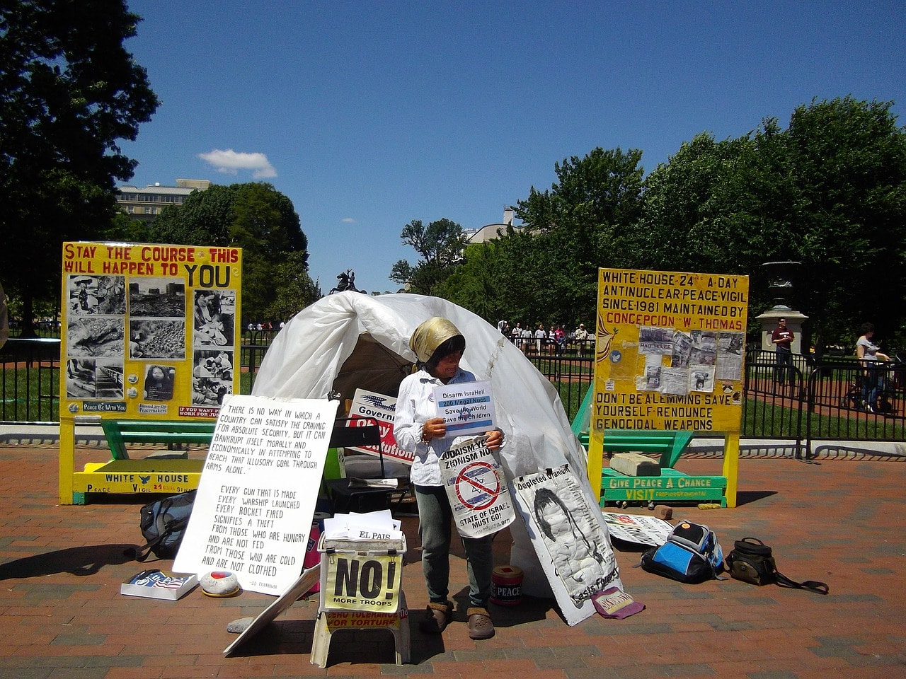 Older white woman standing in front of tent near government building protesting.