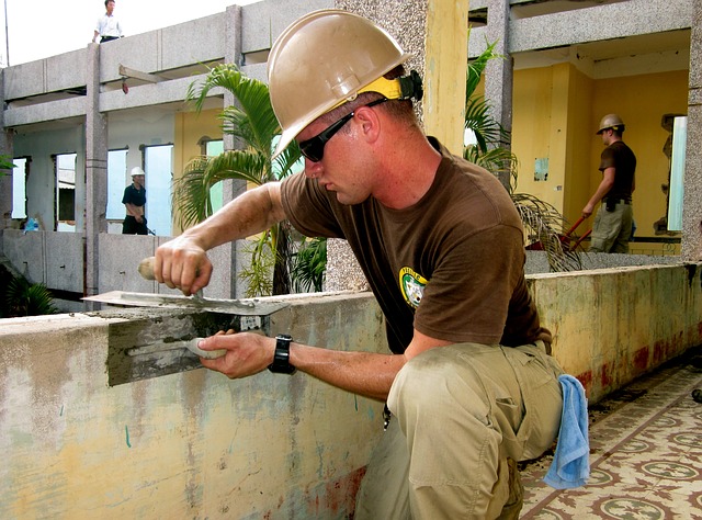 White male laborer building a concrete wall around a building.