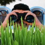 Peeping Tom staring through binoculars while hiding behind grass.