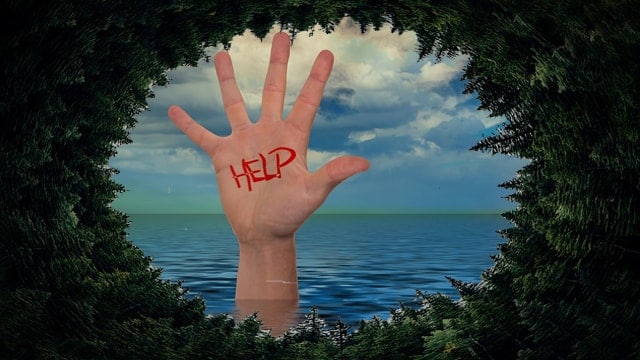 A hand poking up out of the ocean with the word help written in red on his palm.
