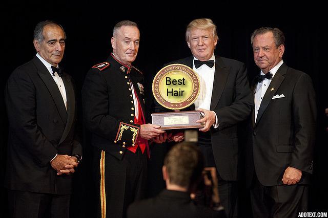 Republican presidential candidate Donald Trump in tuxedo receiving award from businessmen on stage.