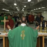 A Catholic priest in a green robe preaching to congregation in church.