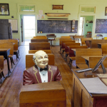 Funny photo of an elderly man sitting at desk in high school classroom.