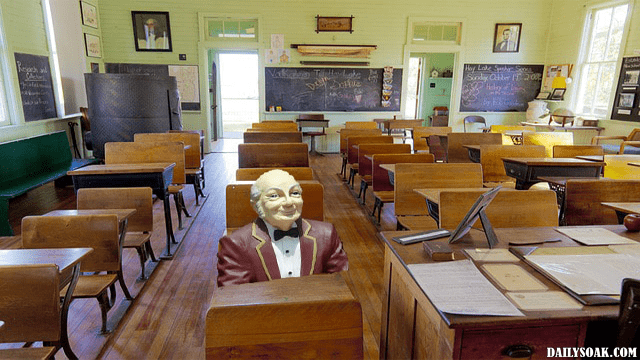 Funny photo of an elderly man sitting at desk in high school classroom.