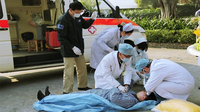 Asian medics working on a dyslexic fat man that had a heart attack on the side of the road.
