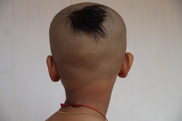 An Indian boy with his back turned showing a small patch of hair on his head.