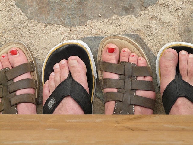 A man and a woman in sandals showing their feet off side by side on a California beach.