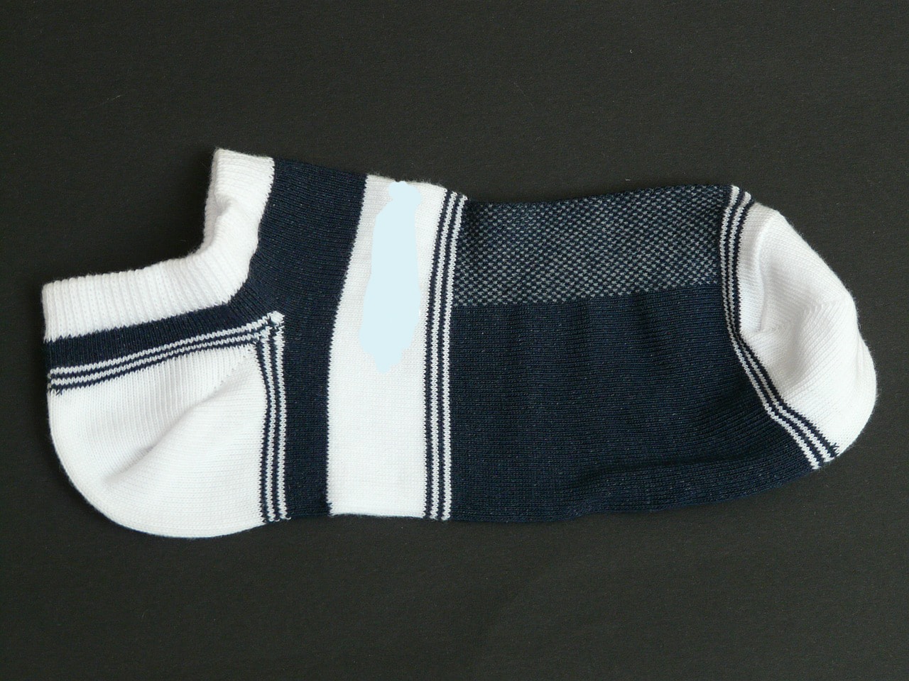 A gray and white Nike ankle sock lying on a bed.