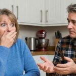 A mute white husband trying to communicate with his white wife at kitchen table.