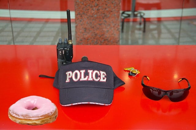 Police hat, sunglasses, and donut on red table.