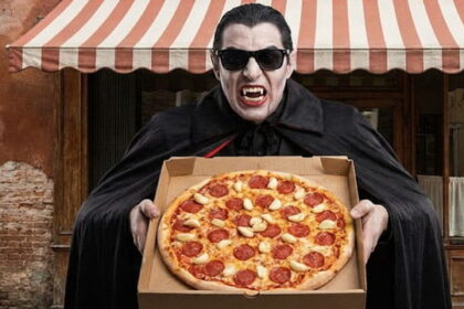 Vampire holding a pizza with a lot of garlic on it in front of a Italian restaurant.