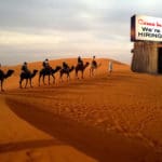 Arabs in robes riding camels in desert.