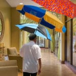 Man in white shirt with open umbrella indoors.