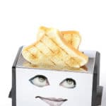 Chrome toaster with eyes and lips staring up at toast.