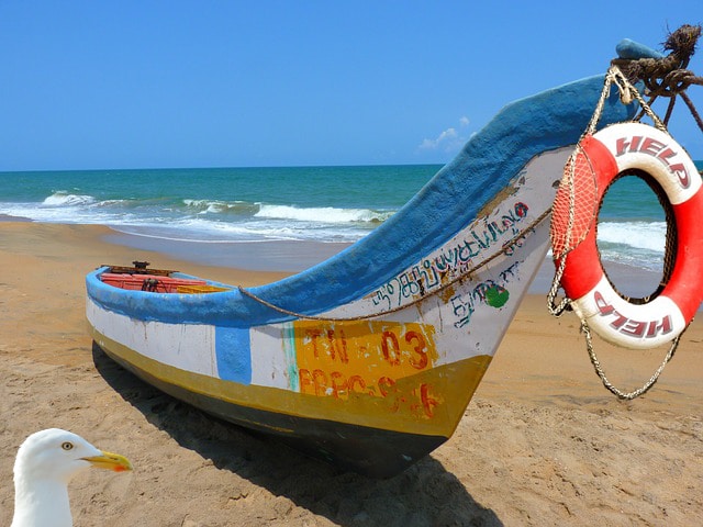 Boat with raft that has help written on it on empty beach.