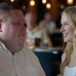 Big guy standing next to a skinny woman inside of a restaurant.