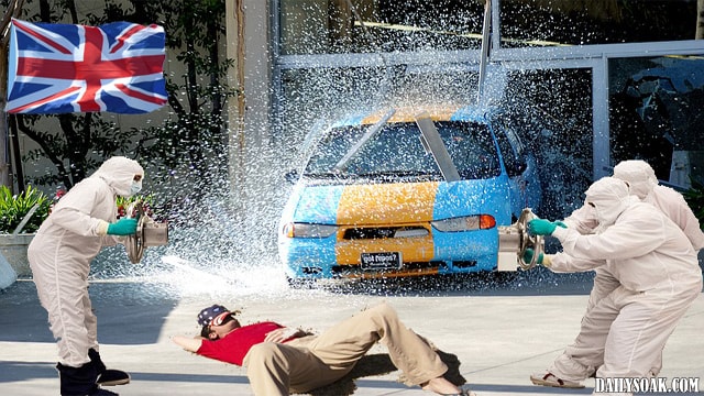 Blue car driving though store window while man lies down on sidewalk.