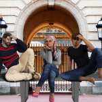 Two UK men and a British woman sitting on bench in front of Buckingham Palace.