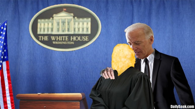 Joe Biden on stage hugging a corn pop wearing black judge's robe.