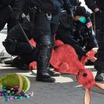 Pink Easter Bunny on ground being arrested by police in riot gear.