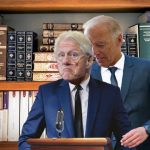 Joe Biden on suit standing behind Bill Clinton in front of book shelf.