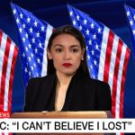 Alexandria Ocasio-Cortez in black shirt standing in front of American flags.