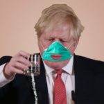 Boris Johnson wearing face mask with mouth hole holding glass.