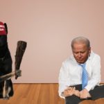 Joe Biden in white shirt sitting on ground near black dog.