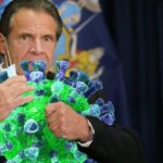Andrew Cuomo wearing blue suit hugging a life-size coronavirus.