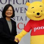 Winnie the Pooh bear standing in front of red, white, and blue Taiwan flag shaking hands with Taiwanese president.