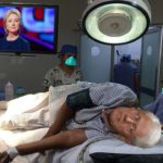 Bill Clinton on hospital bed in front of television.