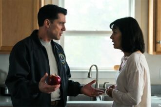 FBI agent wearing blue jacket screaming at scared woman inside kitchen.