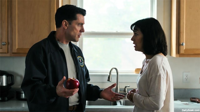 FBI agent wearing blue jacket screaming at scared woman inside kitchen.