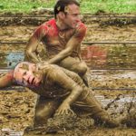 Joe Biden and Emmanuel Macron wrestling in brown mud.