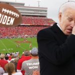Joe Biden wearing black coat and crying inside sports stadium.