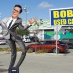 Steven Colbert in gray suit dancing in car parking lot.