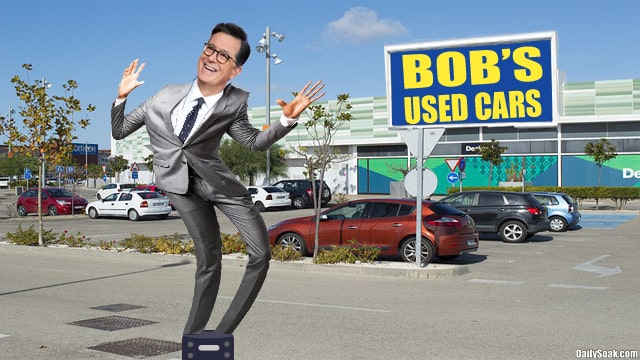 Steven Colbert in gray suit dancing in car parking lot.