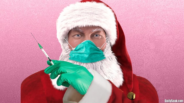 Santa Claus wearing blue face mask while holding a long medical syringe filled with coronavirus vaccine.