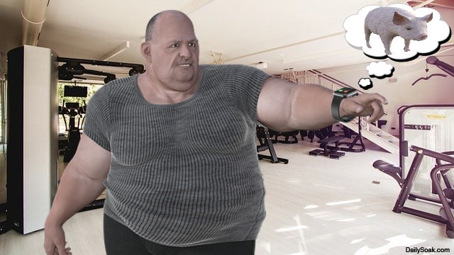 Fat, bald man wearing gray shirt and Amazon Halo inside gym.