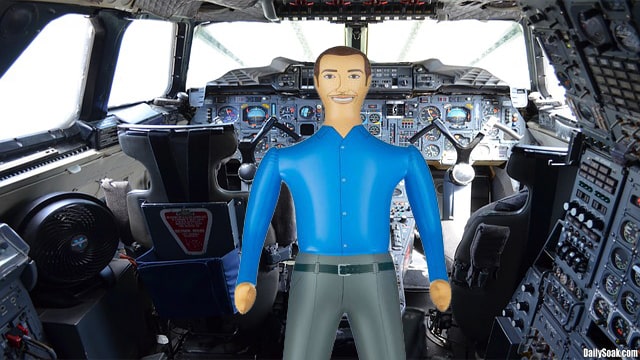 Male United Airlines blow up doll automatic pilot wearing blue shirt and pants inside plane cockpit.