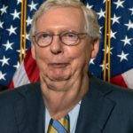 Mitch McConnell wearing blue suit in front of American flag.