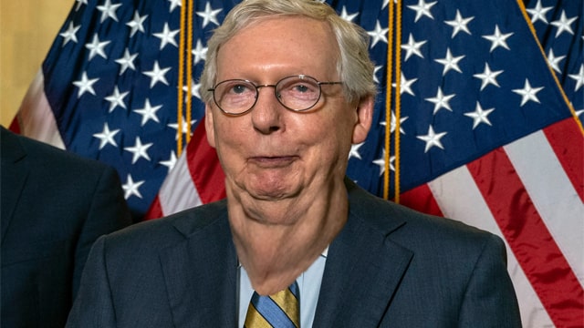 Mitch McConnell wearing blue suit in front of American flag.