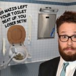 Seth Rogen wearing suit standing inside of white restroom.