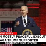 Joe Biden giving speech in front of red White House background.