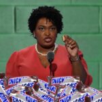 Stacey Abrams eating Snickers bar onstage behind podium while giving speech.