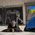 Homeless veteran on street near flag of Ukraine.