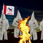 Democrats wearing KKK robes burning fire in dark field.