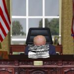 Joe Biden with his head down on Resolute Desk inside Oval Office at White House.